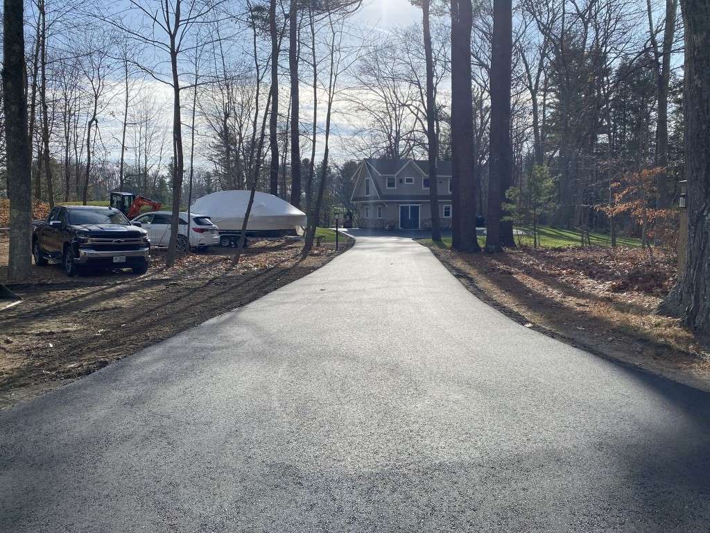 Asphalt driveway leading to a house in a wooded area